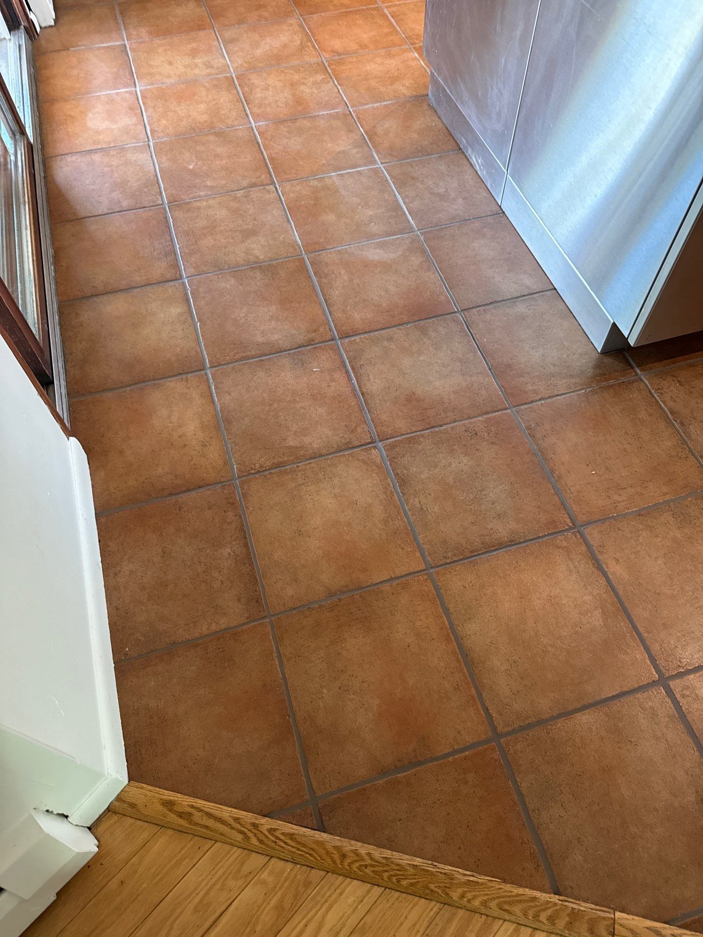 Narrow hallway with beige tiled floor leading to a windowed door and shelves on both sides.