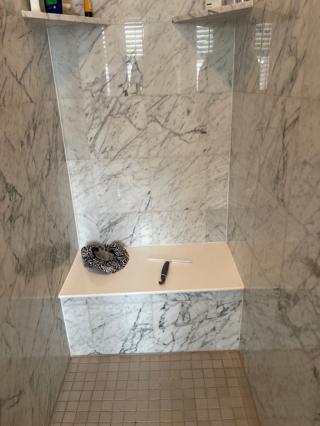 Marble shower stall with bench, towel shelves, and tiled floor; a folded towel and razor rest on the bench.