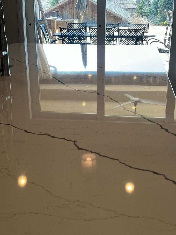 Glossy marble floor with reflected ceiling lights and a large window showing outdoor patio furniture.