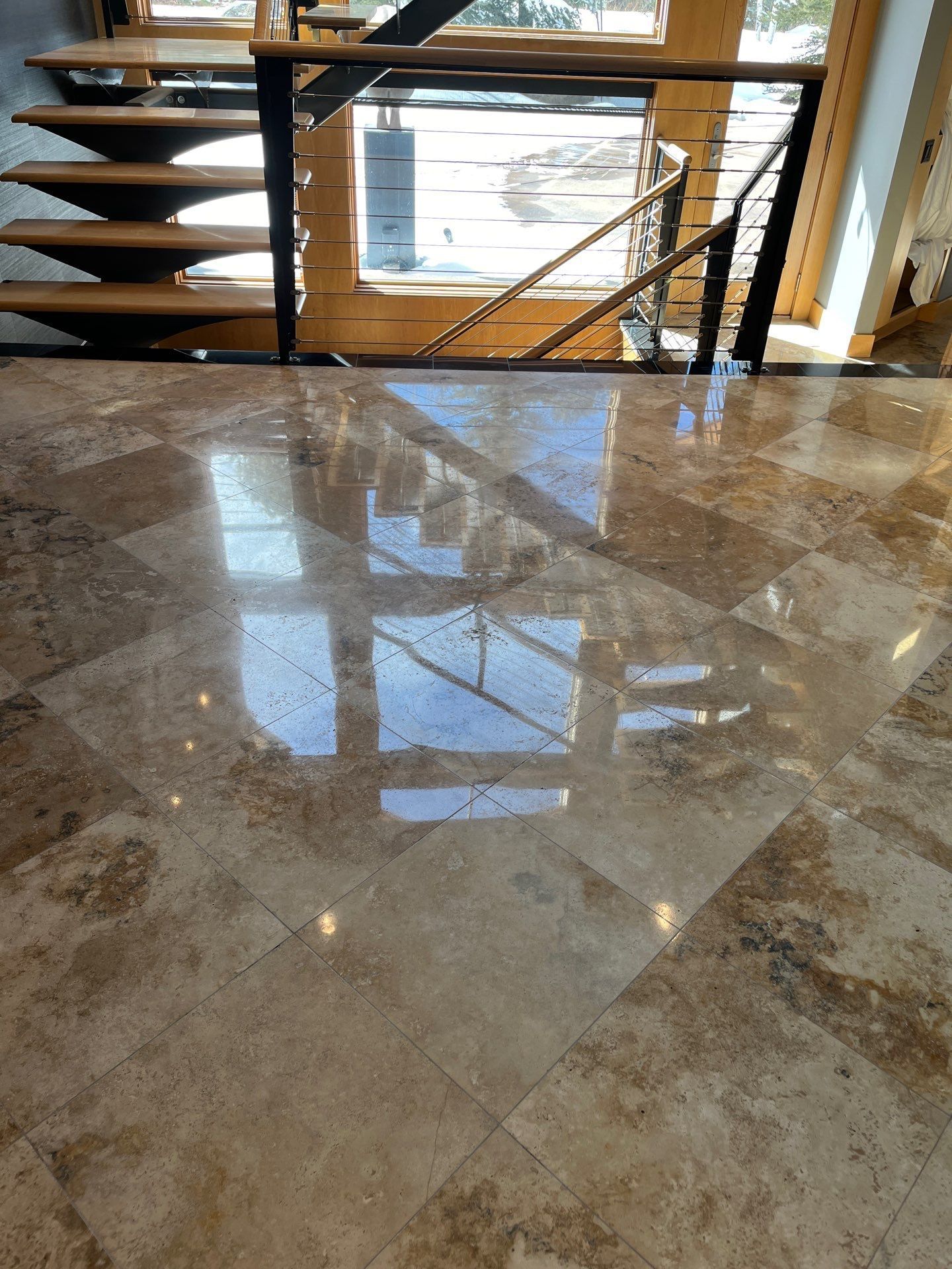 Polished beige stone floor reflecting a window with stairs and a railing in the background.