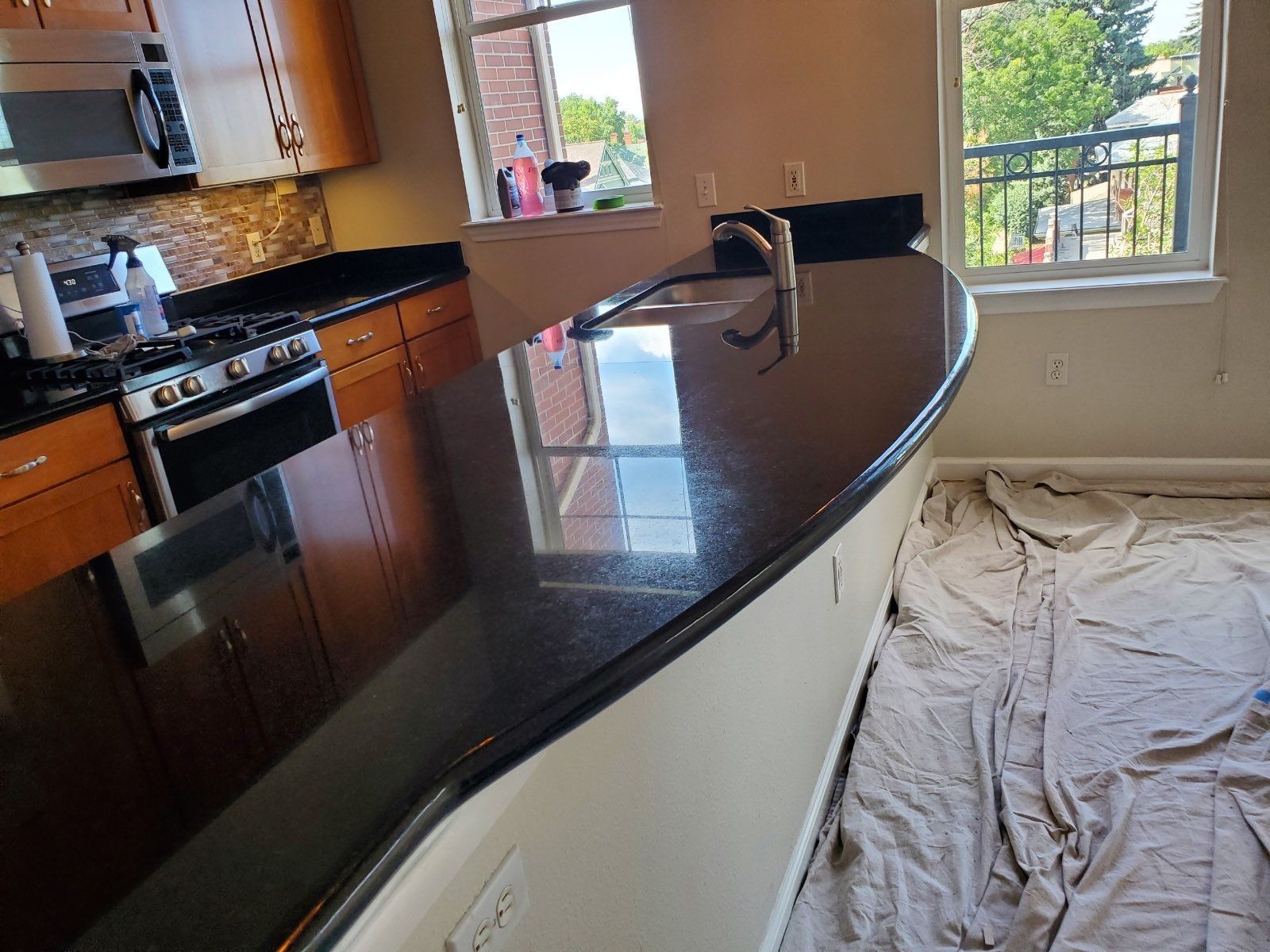 Granite kitchen countertop with sink, faucet, and light reflections near a wall outlet