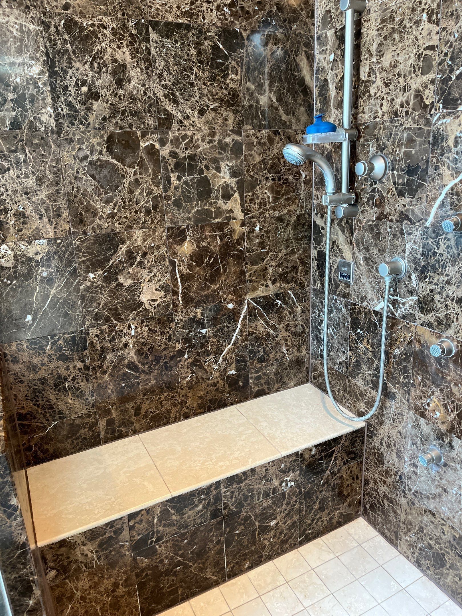 Tiled shower stall with chrome showerhead, built-in shelf, and two faucet handles.