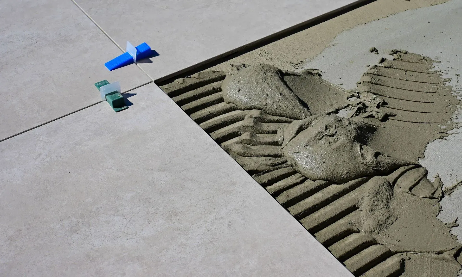 Blue and green tile spacers beside wet mortar spreading over a tiled floor
