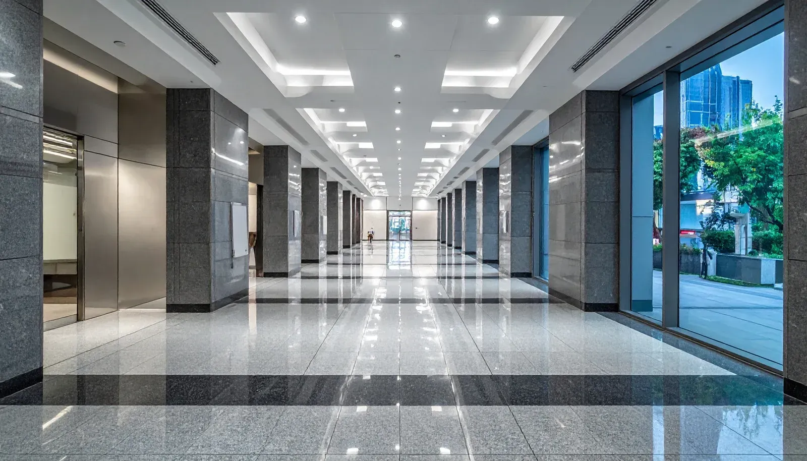 Modern office corridor with polished floors, elevators, and large windows overlooking city buildings