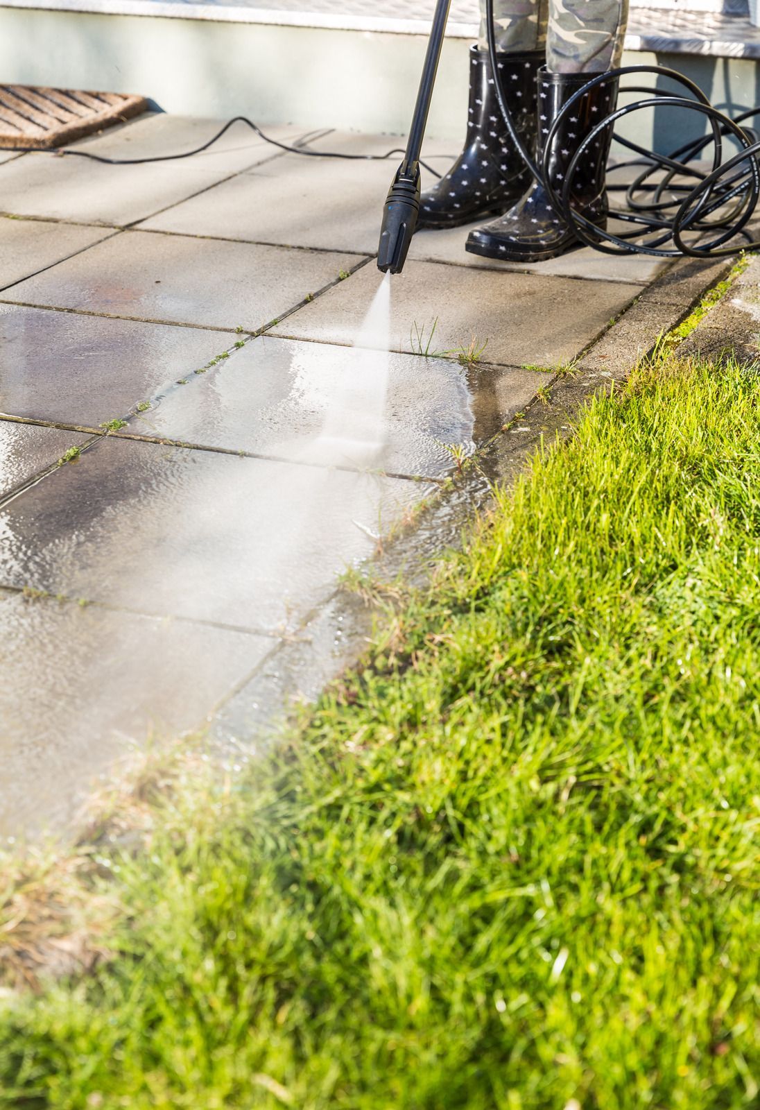 Wet patio paving beside a bright green lawn, with a garden hose and chair legs nearby