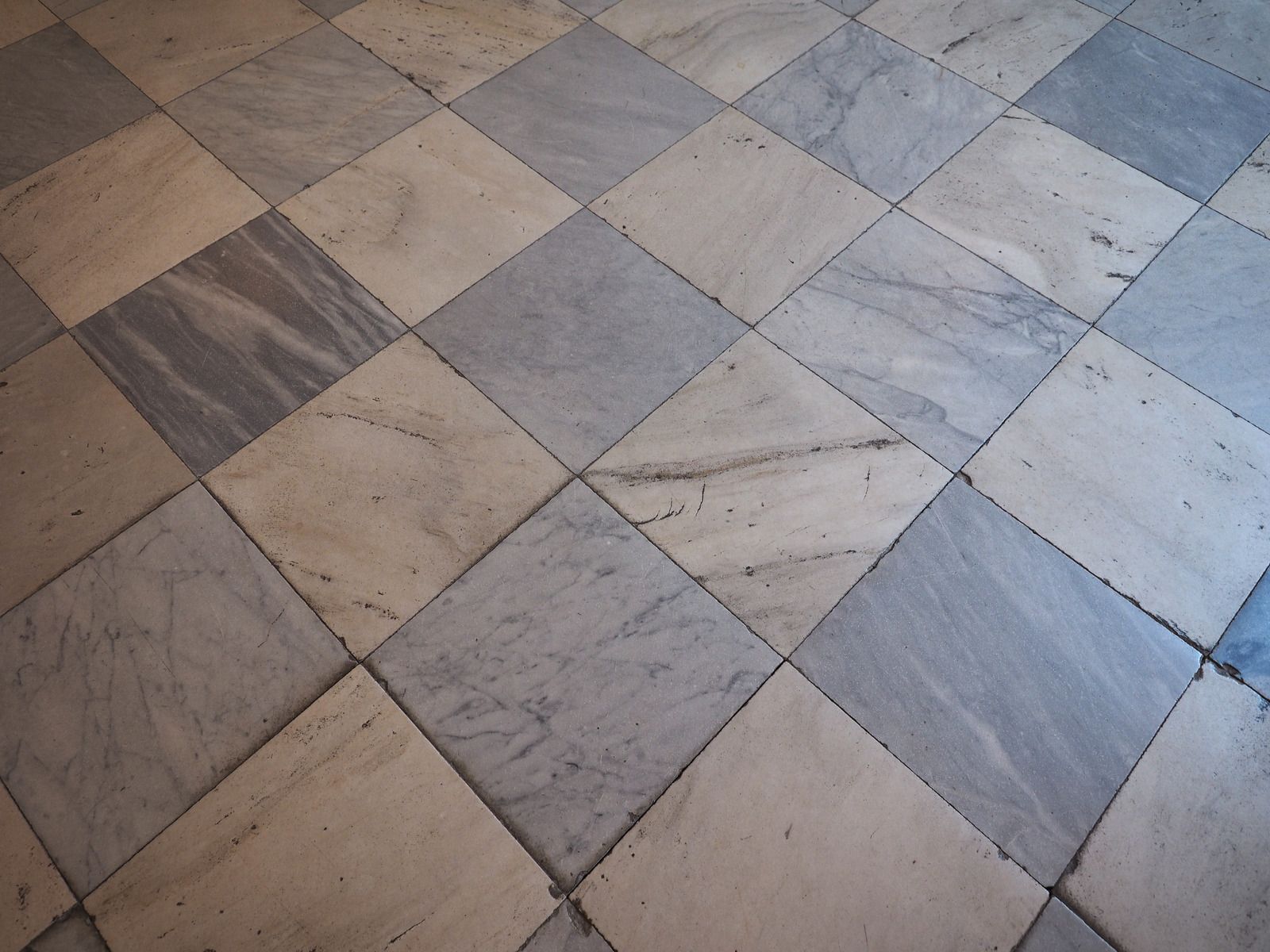 Diagonal pattern of light tan and gray stone floor tiles with subtle wear and dirt