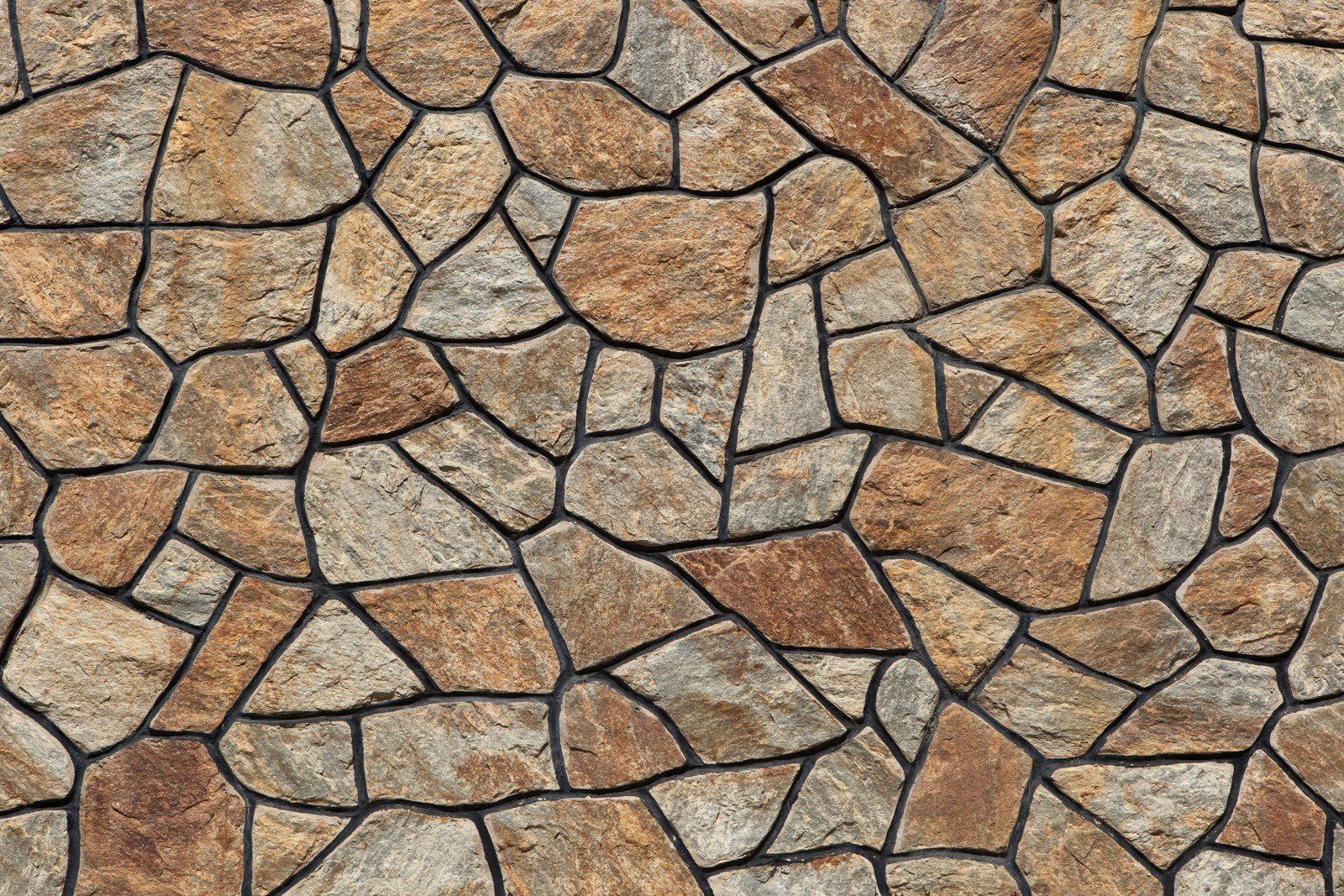 Stone wall with irregular, tan-colored stones separated by dark grout.