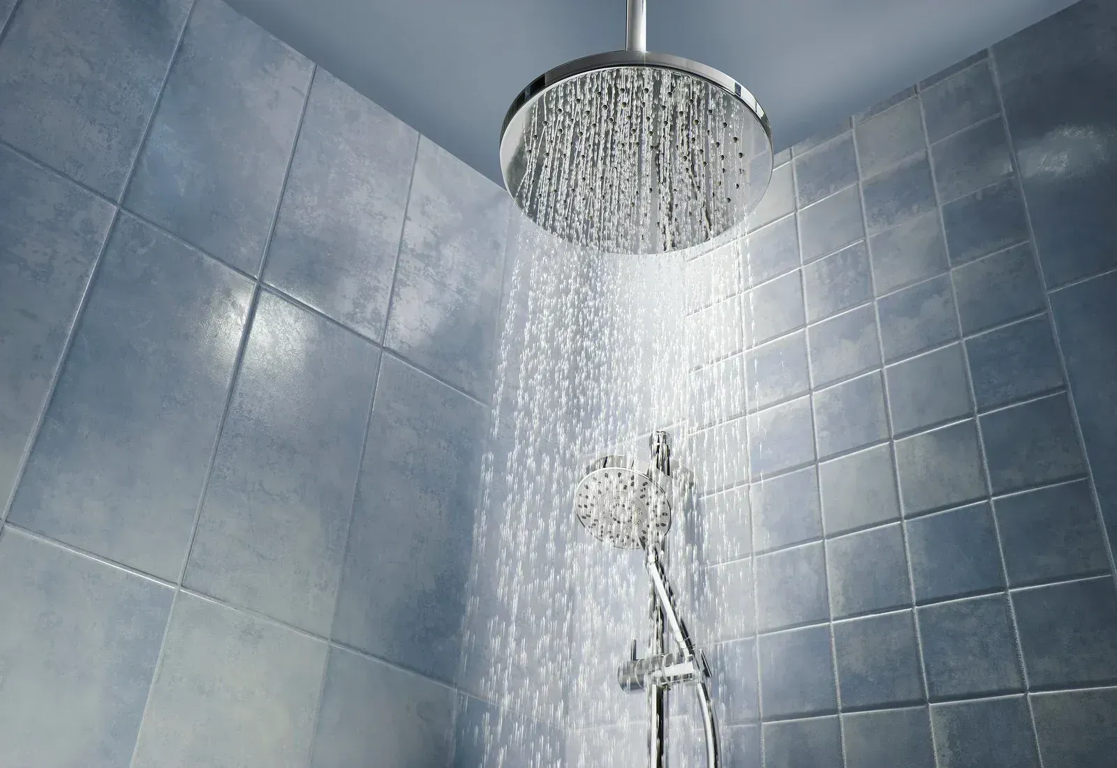 Gray tiled bathroom shower with water running from a round rainfall showerhead.