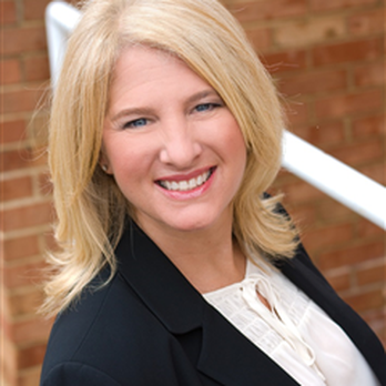A woman in a black jacket and white shirt is smiling