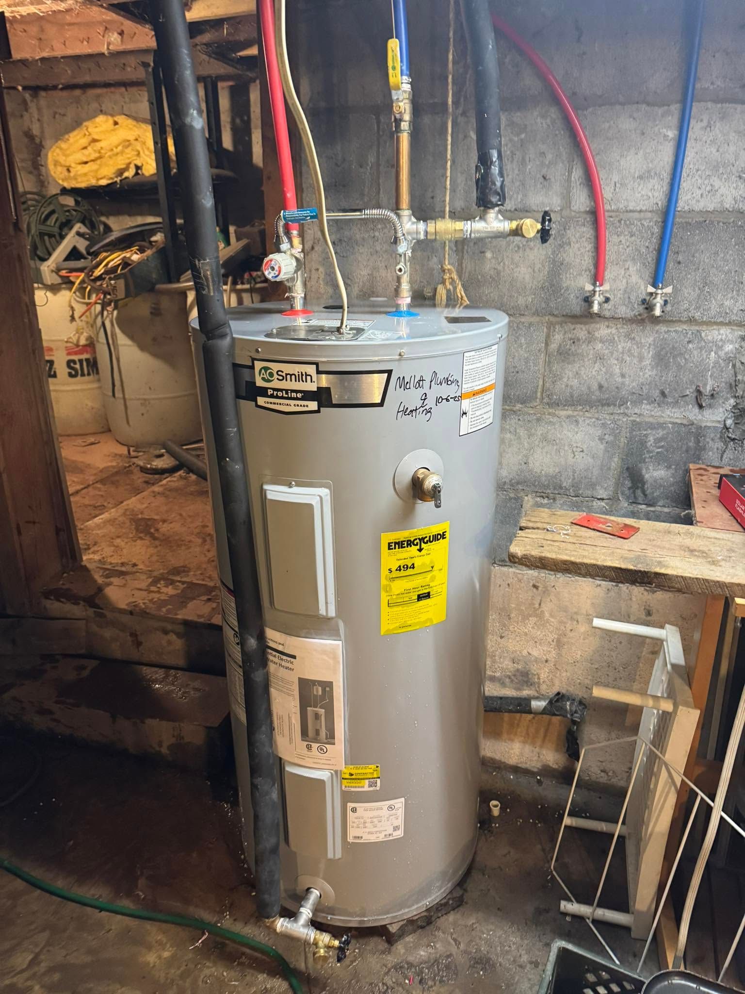 Gray water heater in a basement utility area with exposed pipes and cinder block walls.