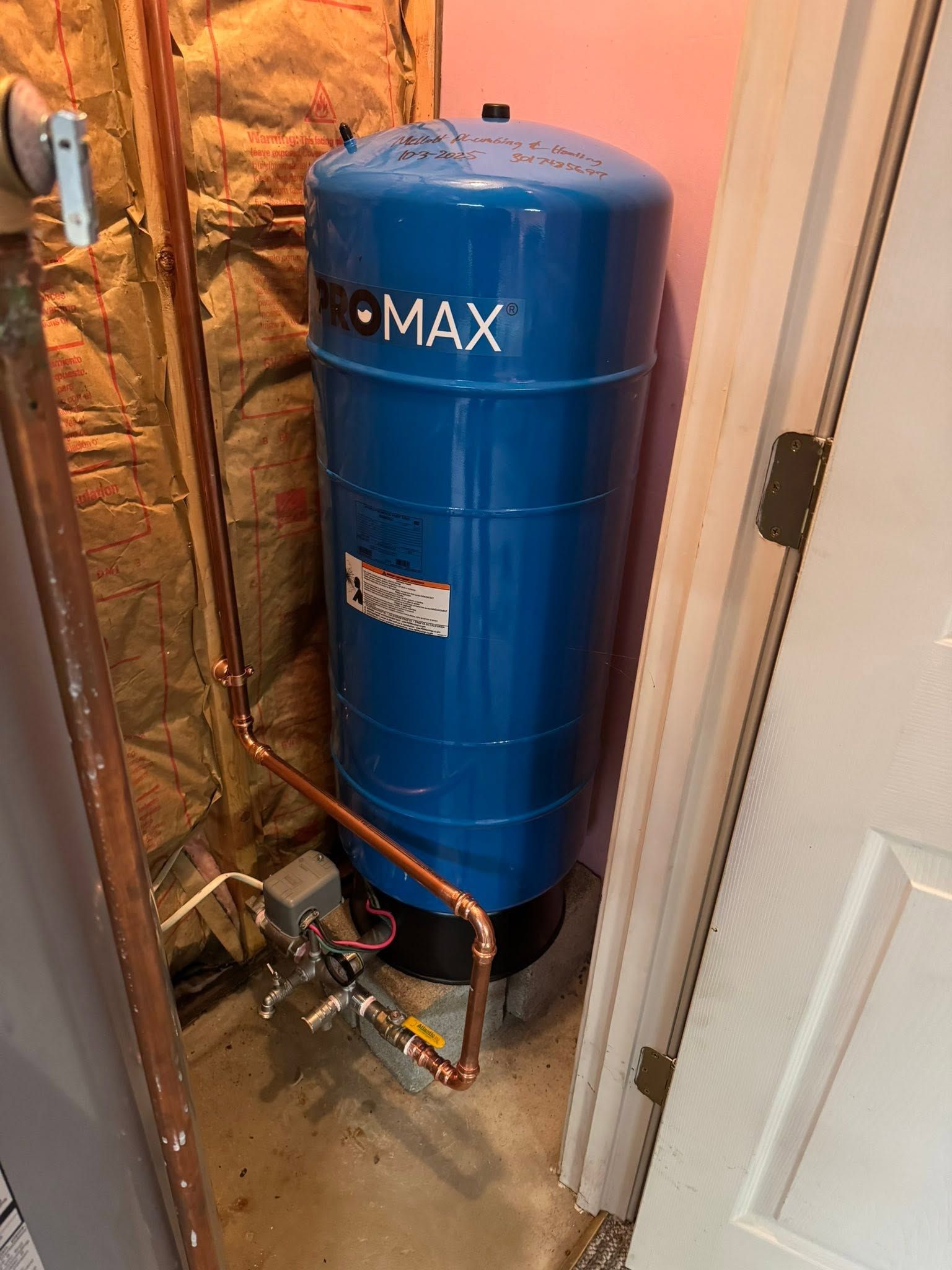 Blue water heater tank in a narrow utility closet beside insulation and a door frame.
