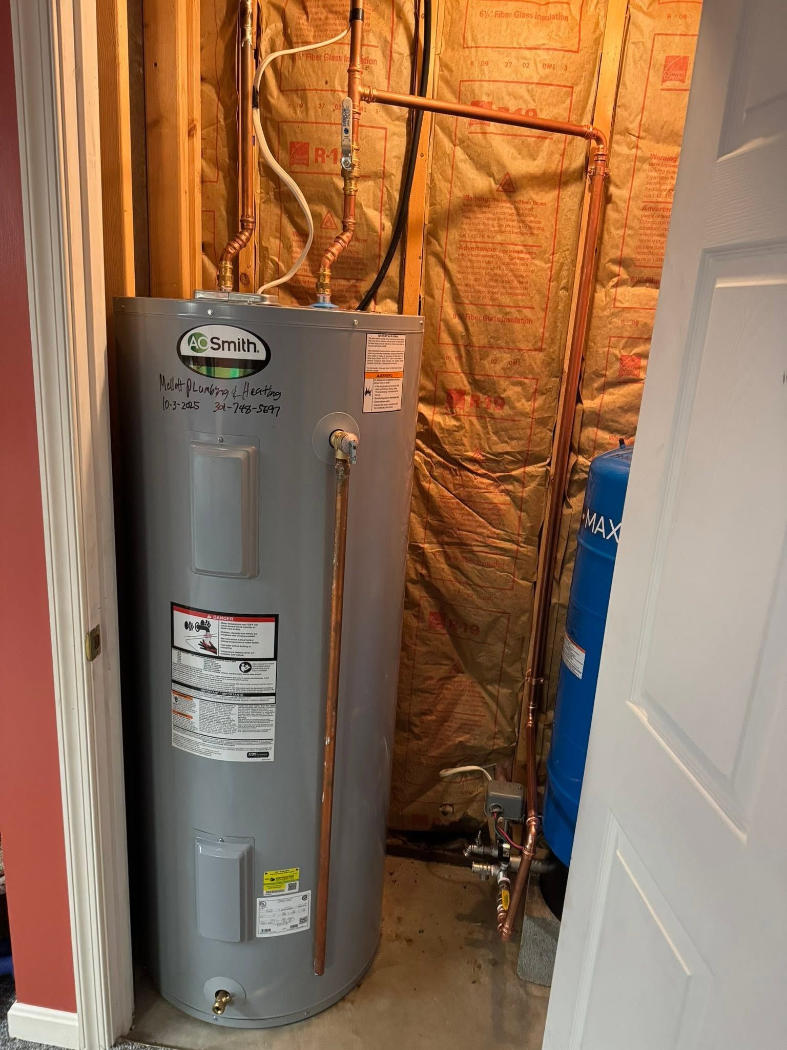 Gray water heater in a utility closet with exposed insulation and open door.