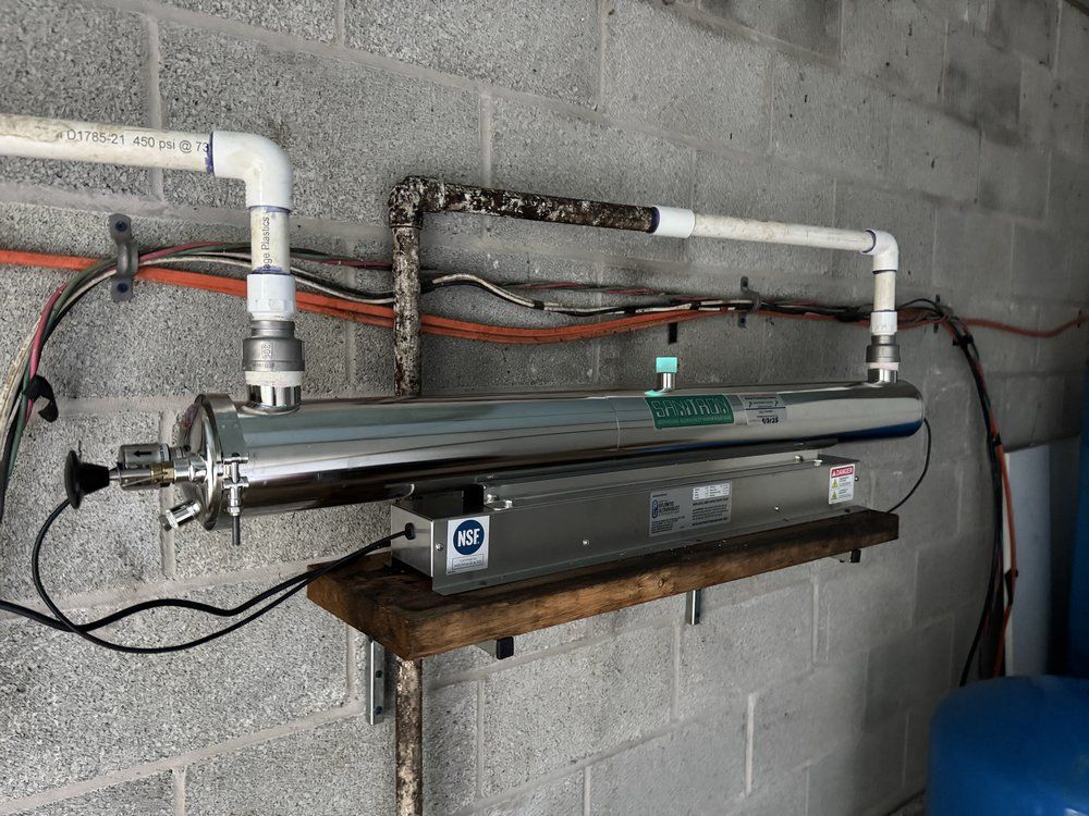 Wall-mounted water heater with white and black plumbing pipes in a cinder block utility room