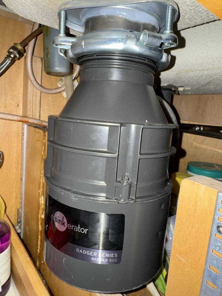 Under-sink garbage disposal unit connected to plumbing beneath a countertop