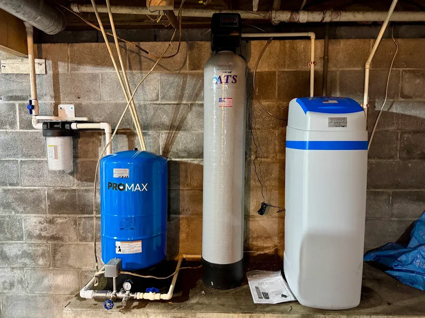 Basement utility area with water treatment tanks, pipes, and a blue pressure tank on a concrete floor