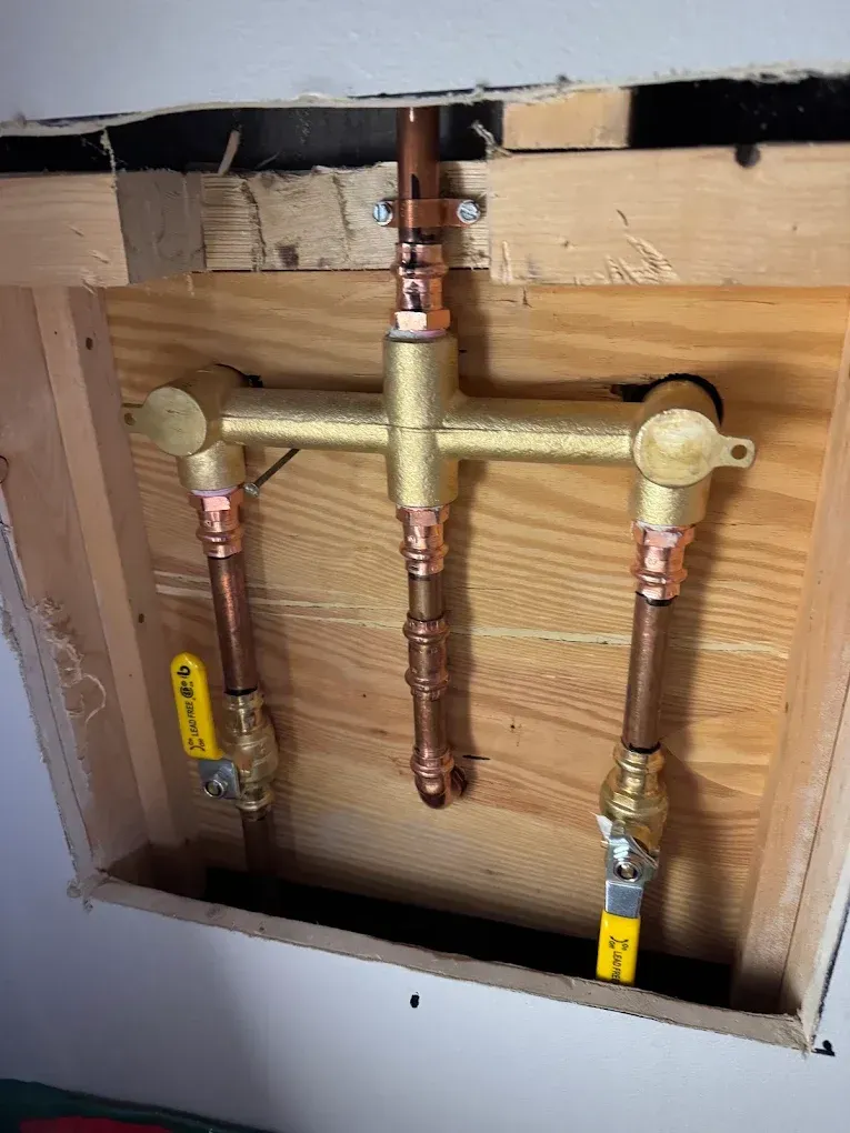 Exposed copper plumbing pipes and valves inside a wall opening under a sink