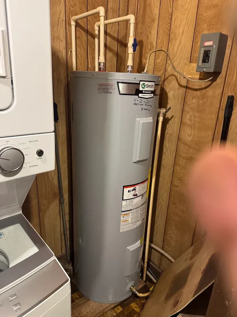 Water heater in a laundry/utility closet with exposed pipes and a washer nearby.