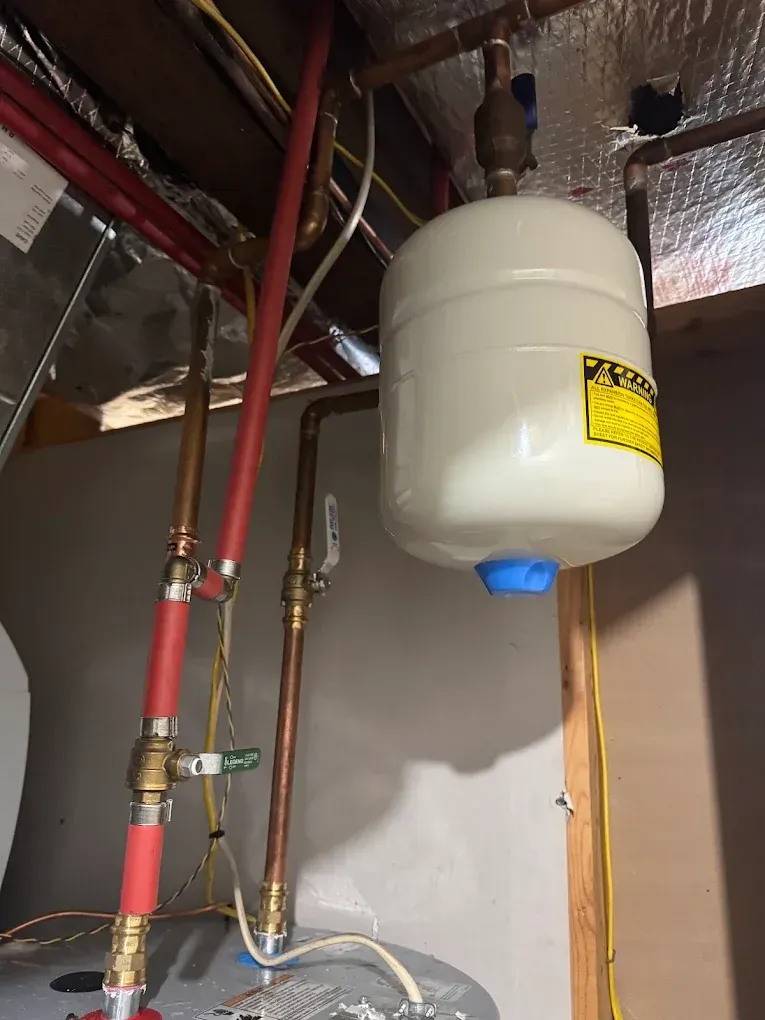 White pressure tank and exposed plumbing pipes in a basement utility area