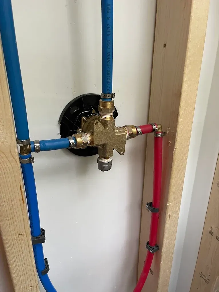 Plumbing valve assembly with blue and red pipes on a white wall, showing a brass control valve.