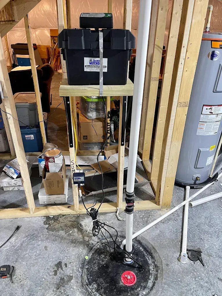 Utility equipment in exposed wall framing beside a water heater, with a small floor leak and wet area.
