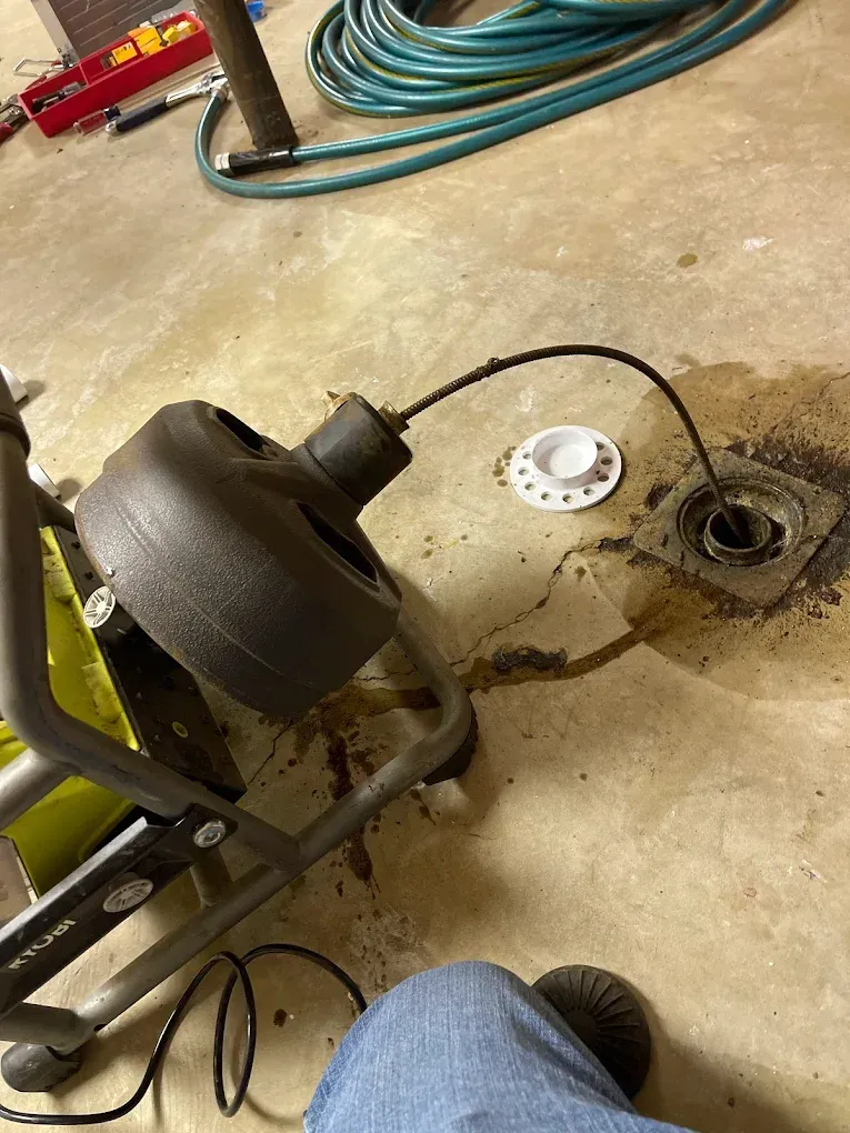 Worklight on a concrete garage floor beside a drain, hose, and coiled extension cord