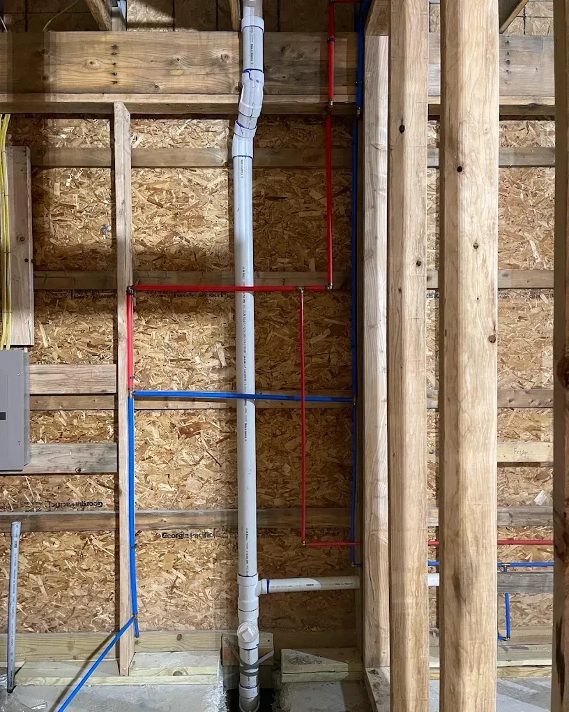 Exposed wall framing with red and blue pipes and gray ductwork in a construction site