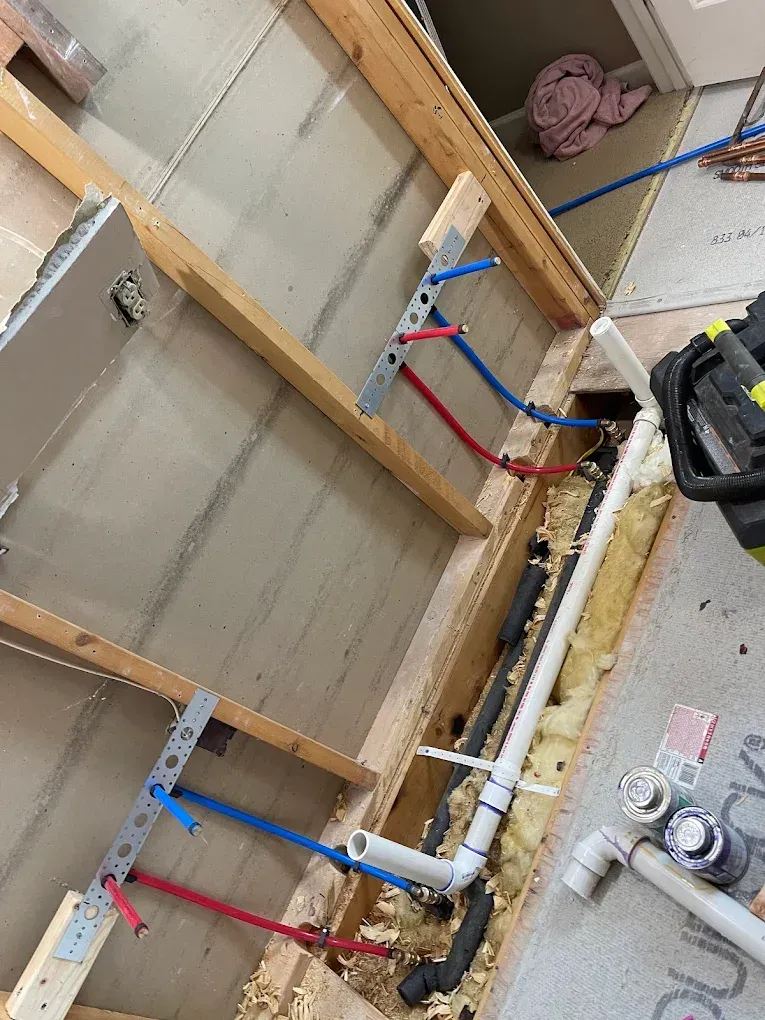 Exposed plumbing and shutoff valves on a wall under construction, with blue and red pipes and a drill nearby