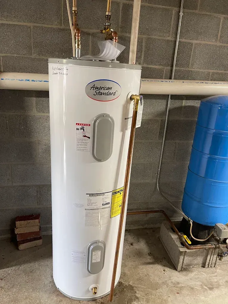 White water heater tank in a utility room beside a blue tank against a concrete block wall