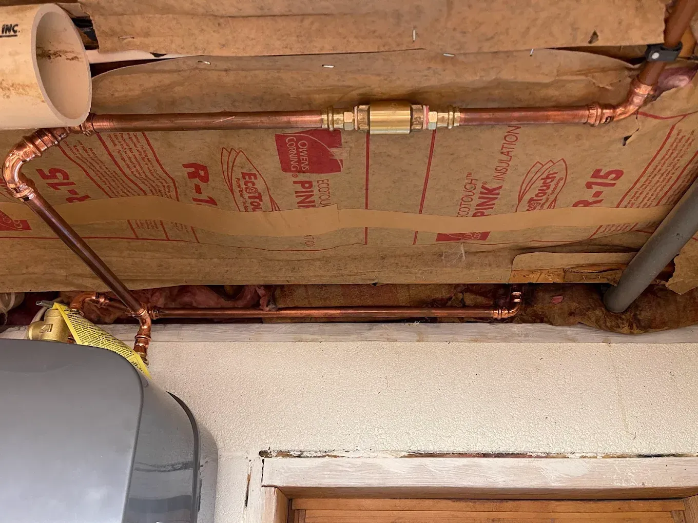 Exposed ceiling insulation and copper pipes above a doorway in a utility area