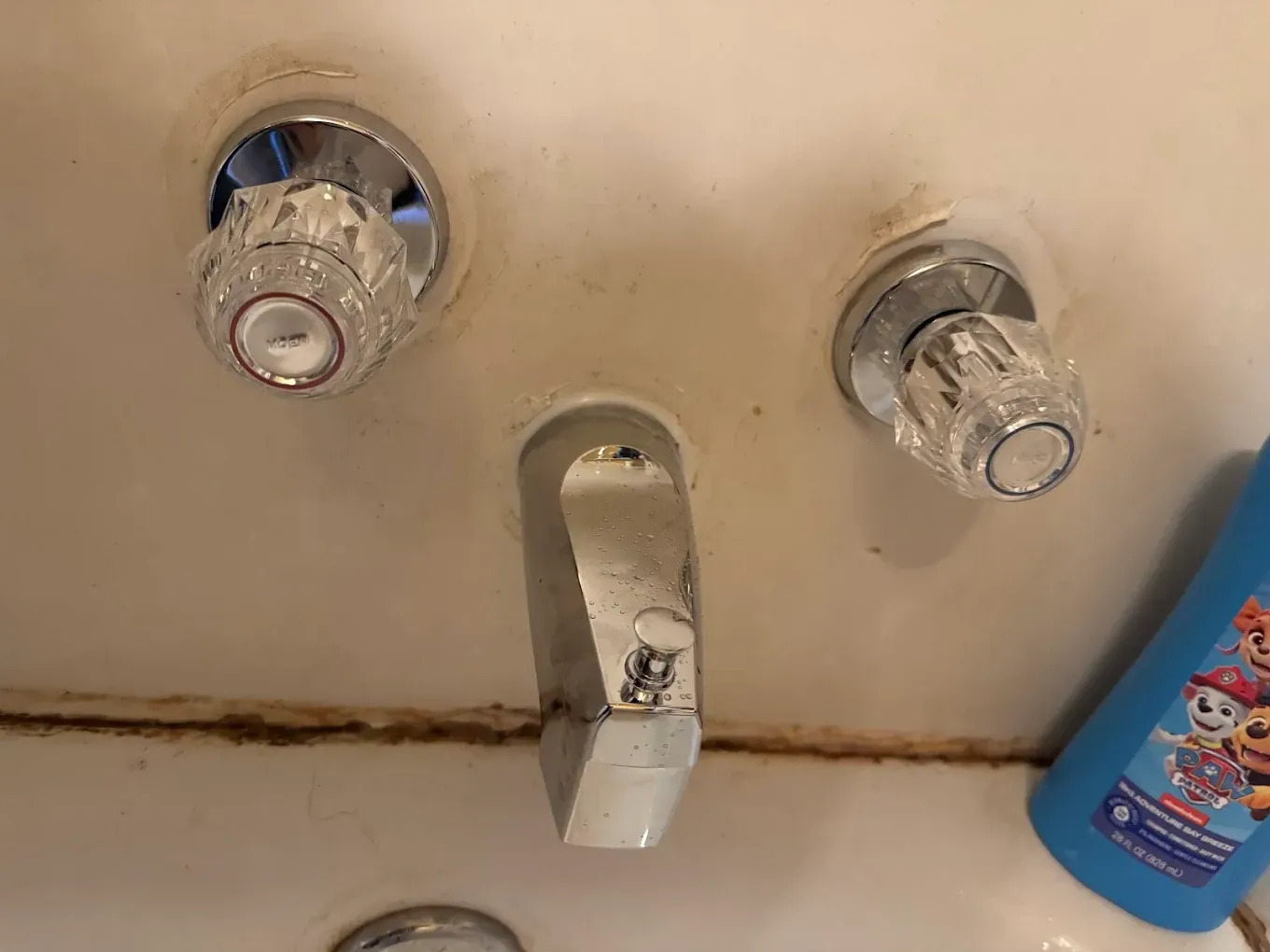 Bathroom sink faucet with two clear knobs and a soap bottle at the right edge.
