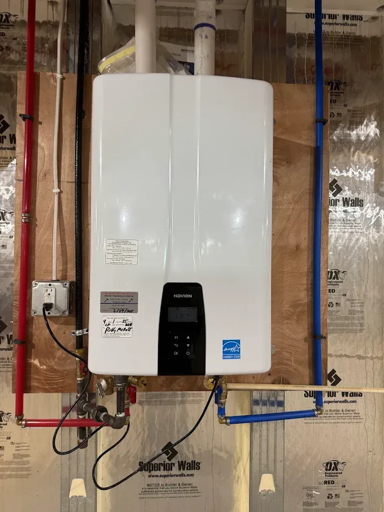 White wall-mounted water heater with exposed pipes and wires in an unfinished utility room