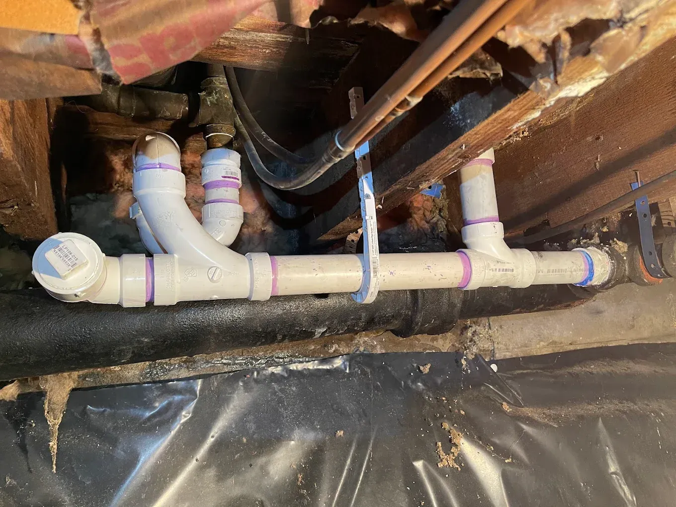 PVC plumbing pipes and fittings installed beneath a floor joist in a crawl space