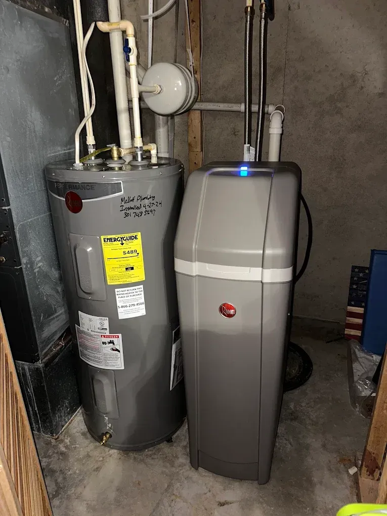 Two gray water heaters in a basement utility area, with pipes and a blue indicator light on one unit.
