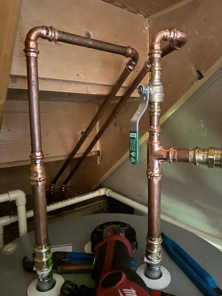 Copper plumbing pipes and valves under an attic floor, with a red pump below.