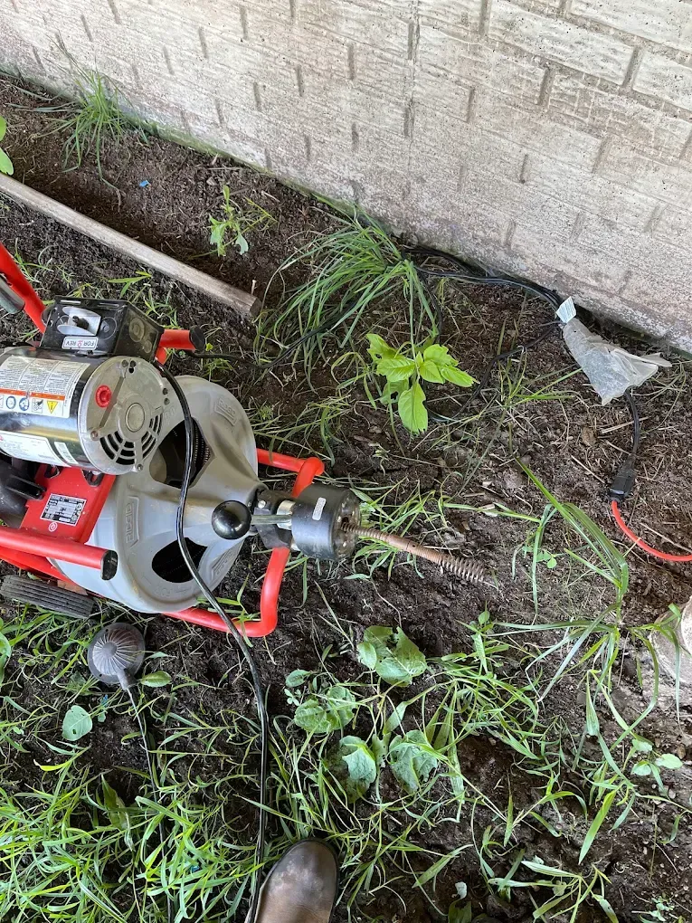 Red lawn tool beside a brick wall, cutting overgrown weeds in a dirt strip.