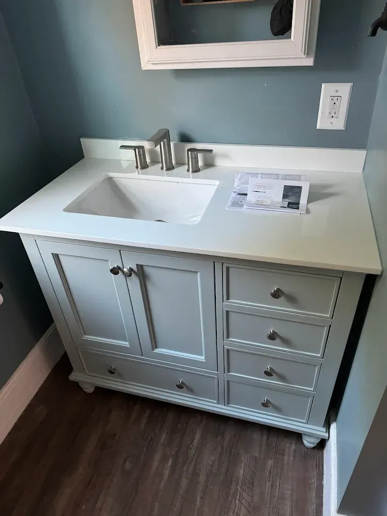 White bathroom vanity with sink, chrome faucet, mirror, and drawers against blue walls