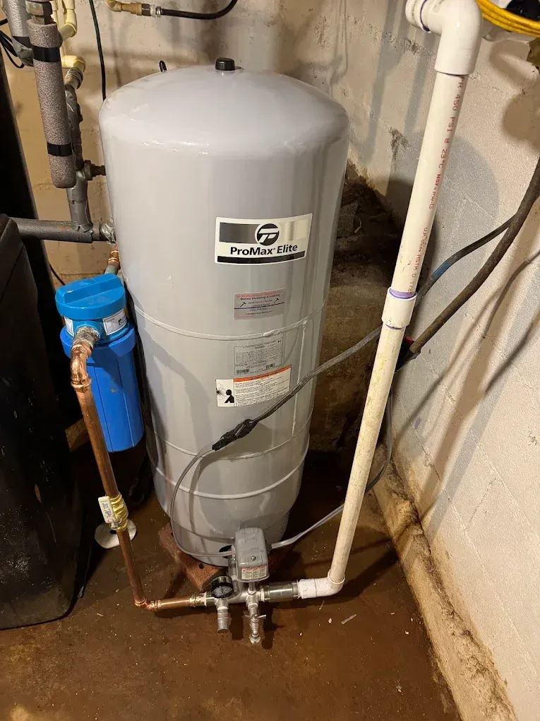 Gray water heater with pipes and a blue filter in a utility room.
