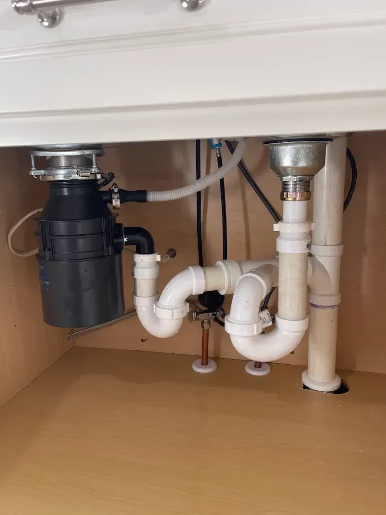 Under-sink plumbing with white pipes, a black disposal unit, and chrome drain fittings under a countertop