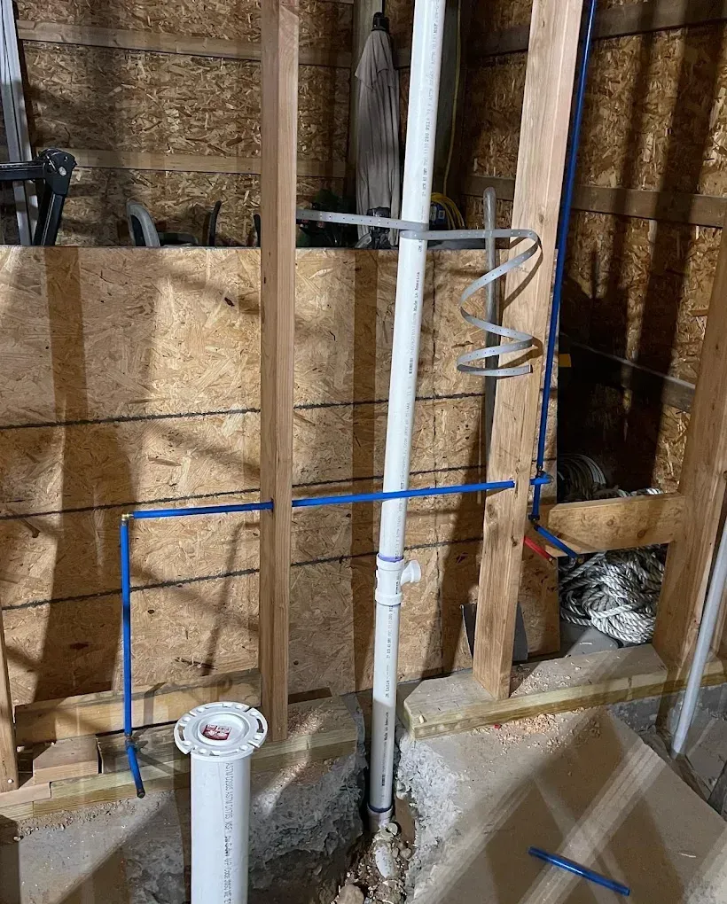 Exposed plumbing and framed wall in a construction site, with pipes, wiring, and insulation visible.