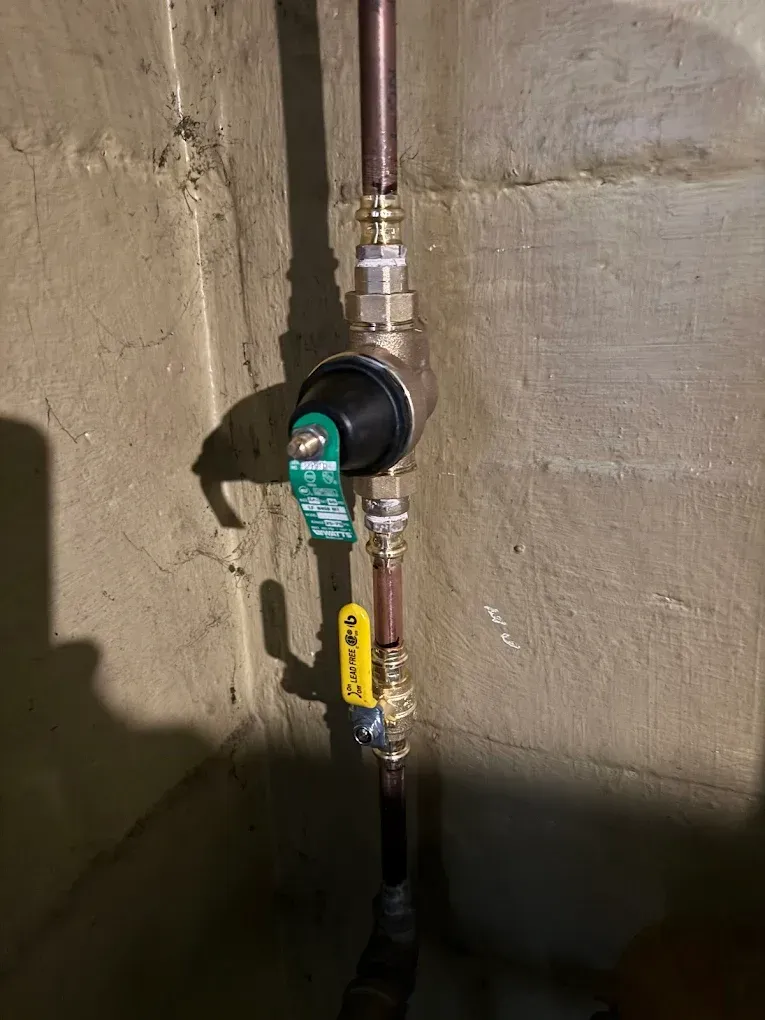 Wall-mounted water pipes with a green and yellow shutoff valve on a concrete wall.