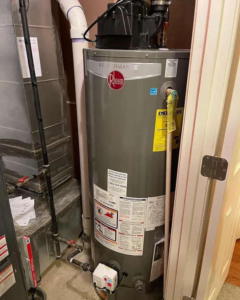 Gray water heater in a utility closet with pipes and labels nearby