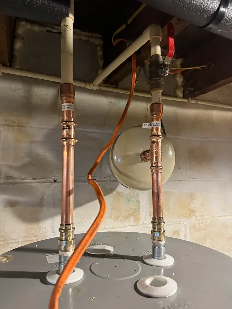 Under-sink plumbing with two copper pipes, white fittings, and an orange hose against a wall
