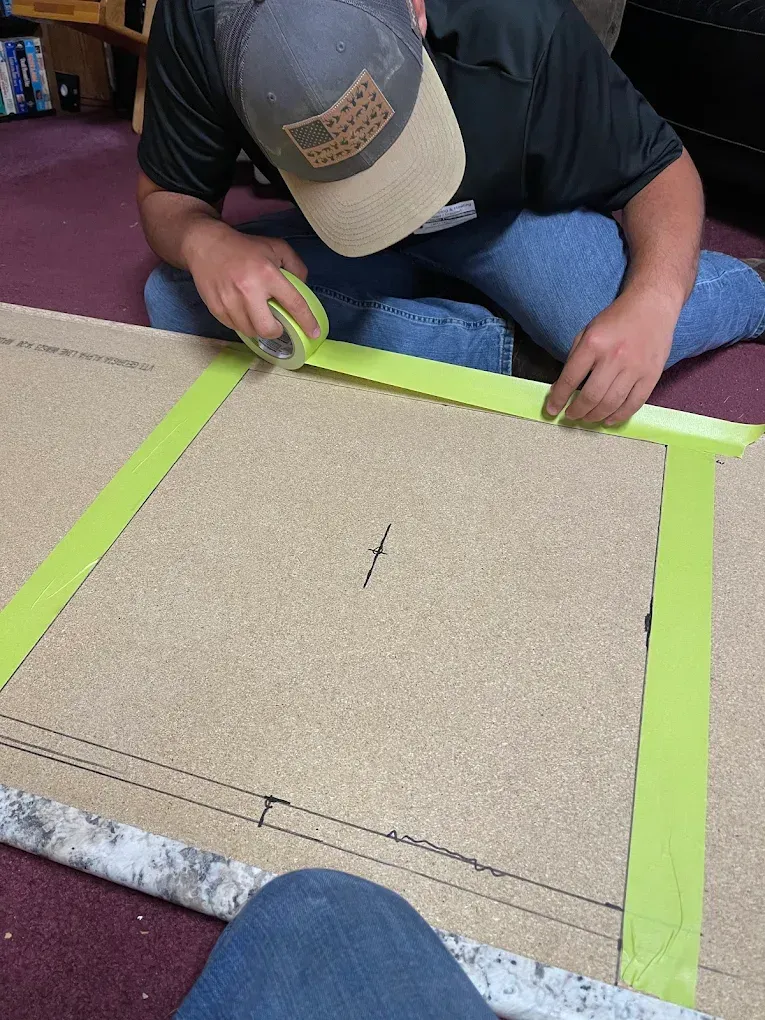 Person measuring and taping a large cardboard piece on the floor.