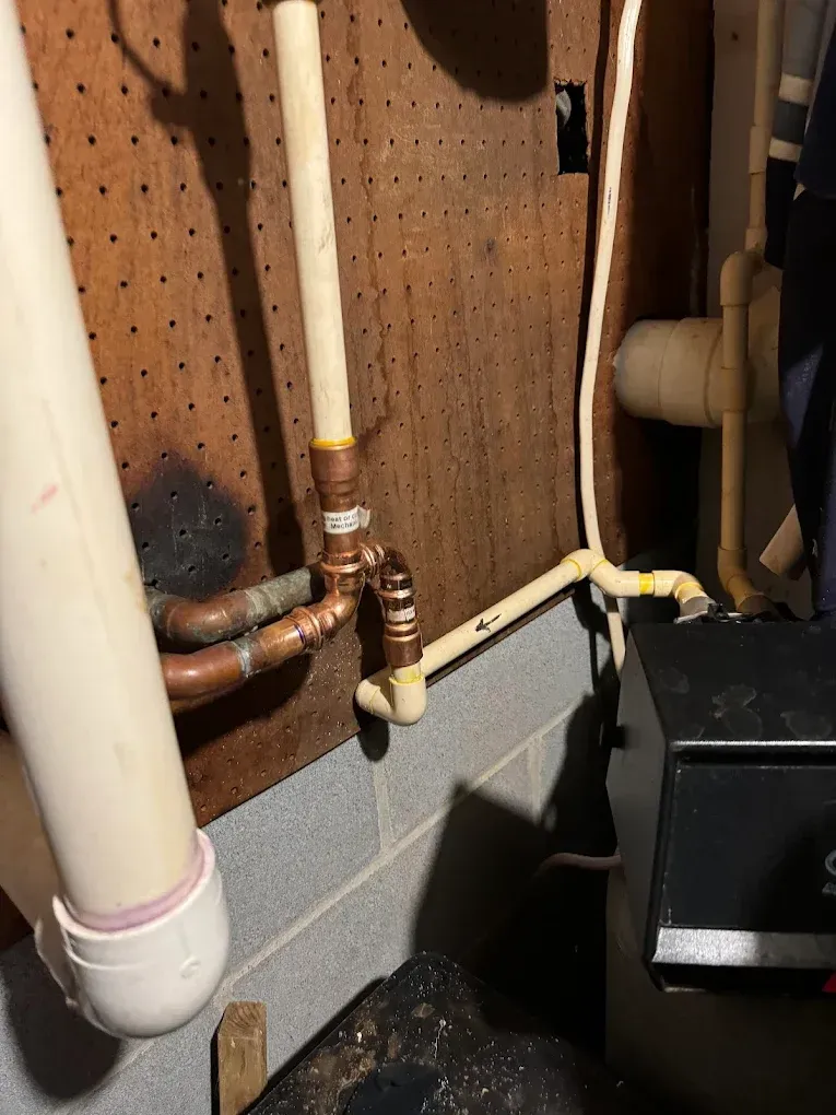 Copper and PVC plumbing pipes against a pegboard wall in a basement utility area.