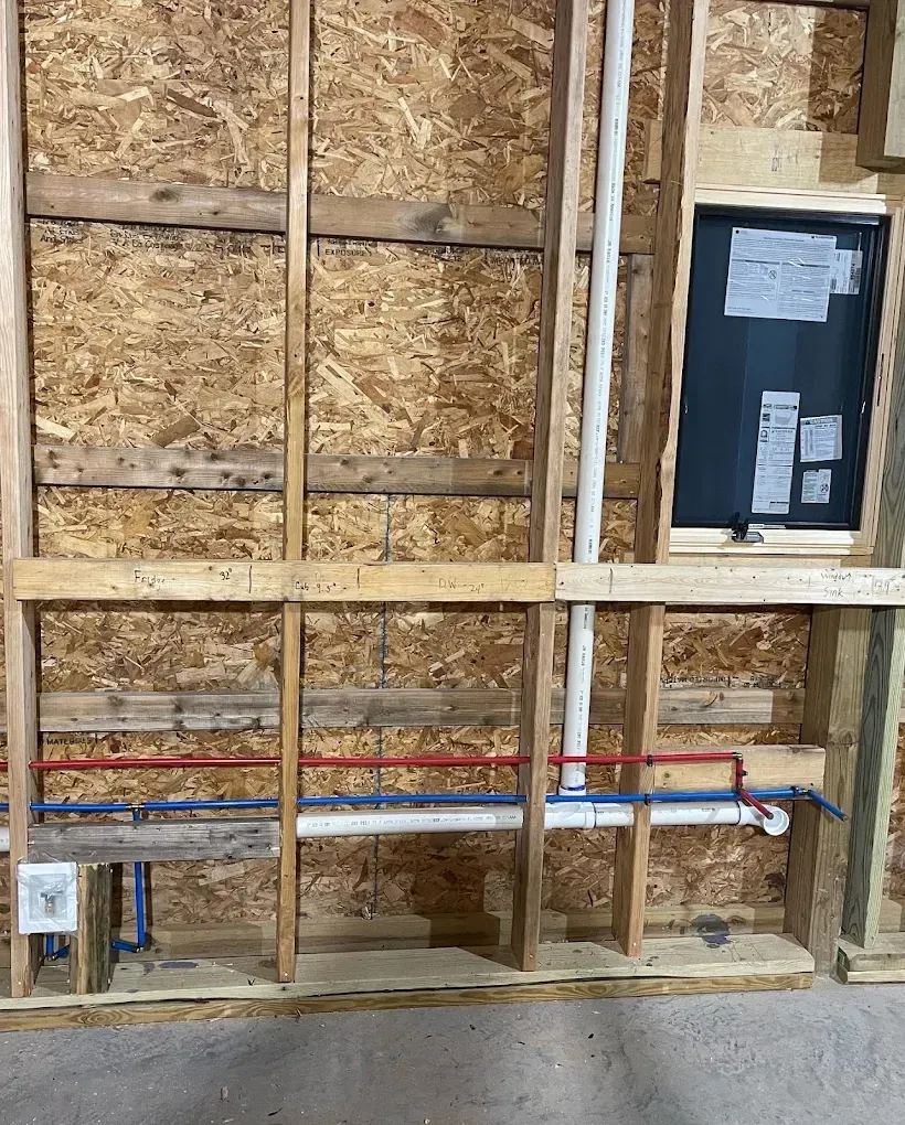 Exposed wall framing with red and blue pipes and an electrical panel in a construction area