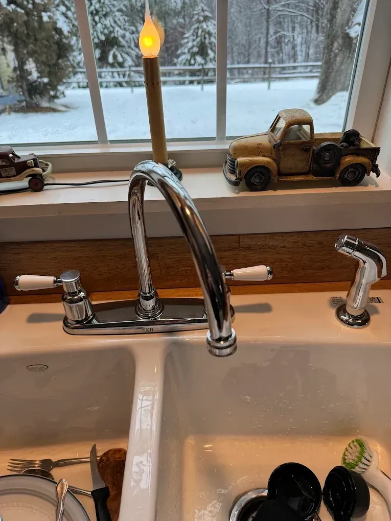 Kitchen sink with chrome faucet, dish soap, and toy truck on the windowsill by a snowy window