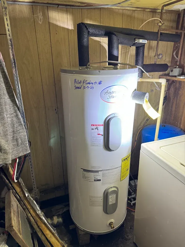 White water heater in a utility closet with pipes and a laundry machine nearby.