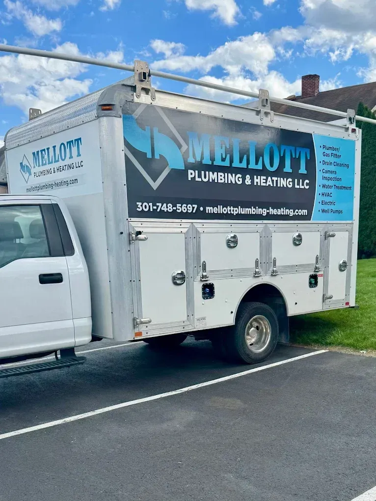 White Mellott plumbing truck parked beside a house under a cloudy blue sky.