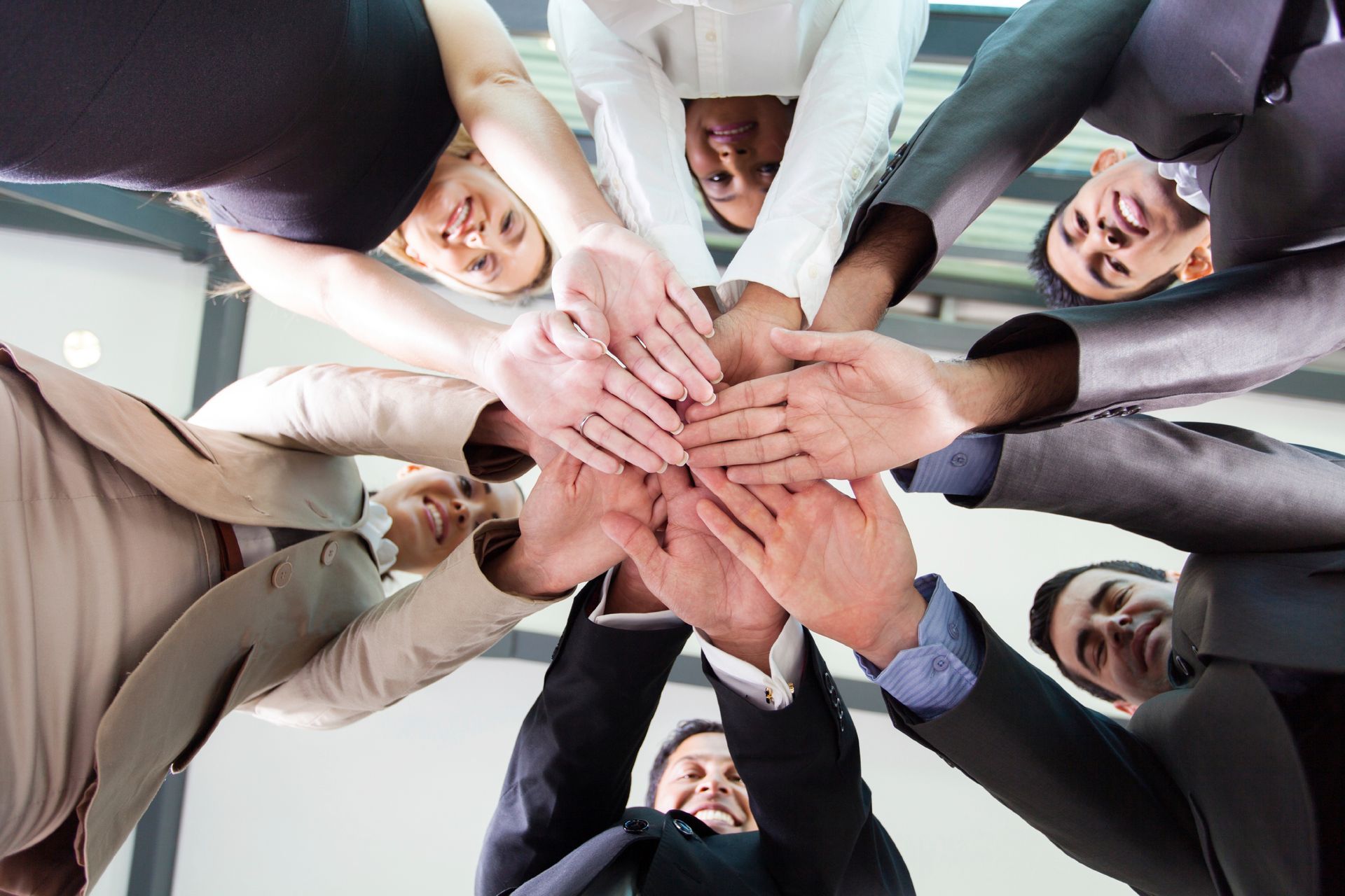 People in business attire with hands together in a circle, symbolizing teamwork.