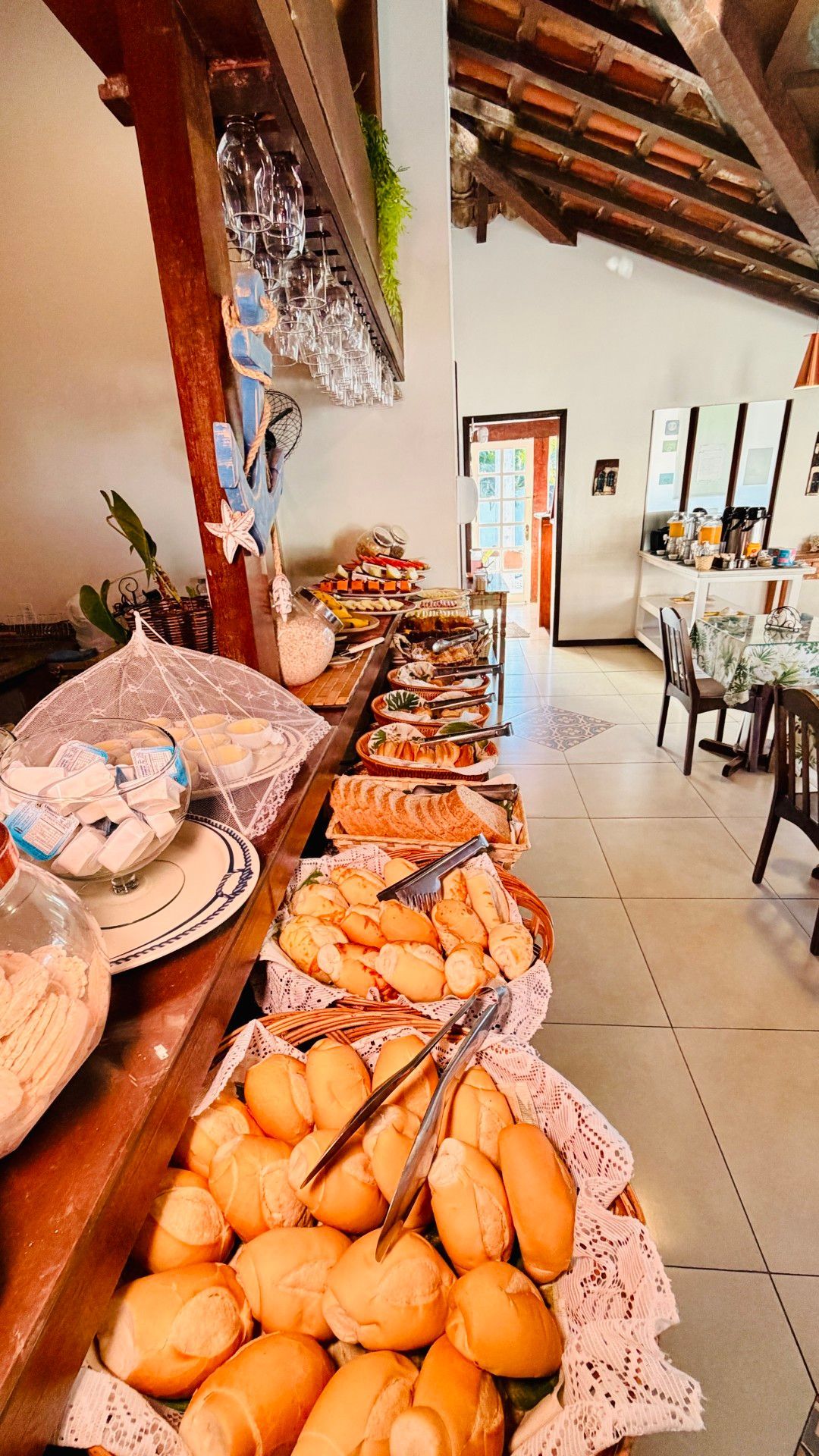 Bandeja com diversos pães e produtos de pastelaria numa padaria iluminada, com vigas de madeira no teto